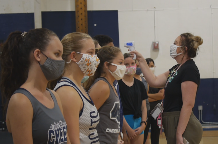 Coach Kaitlyn Hoskins performs a temperature check on the cheer squad before practice.