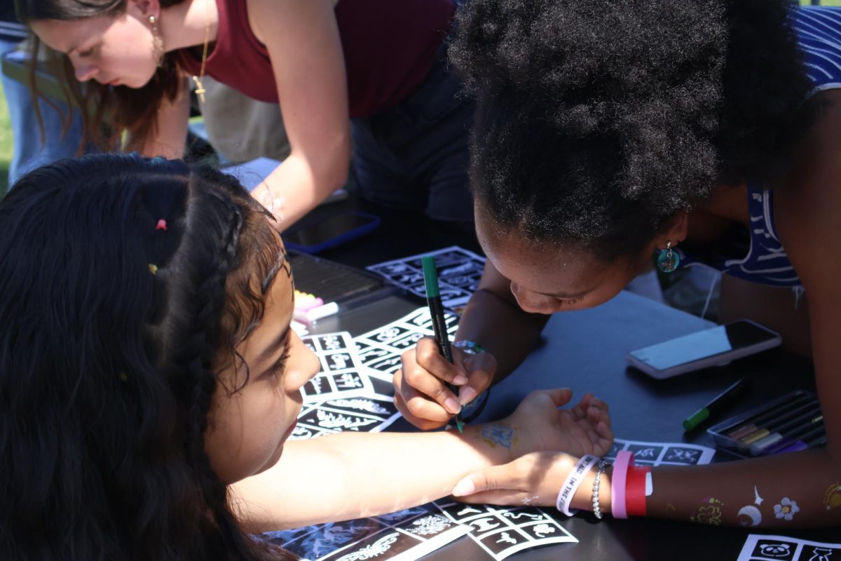 Junior Jaelyn Lettsome draws a design on a student's arm. “I’ve been making tattoos the whole time and we’ve had a good amount of people come by,” Lettsome said. “The officers set this up so we could use our art skills and share them with the school.”