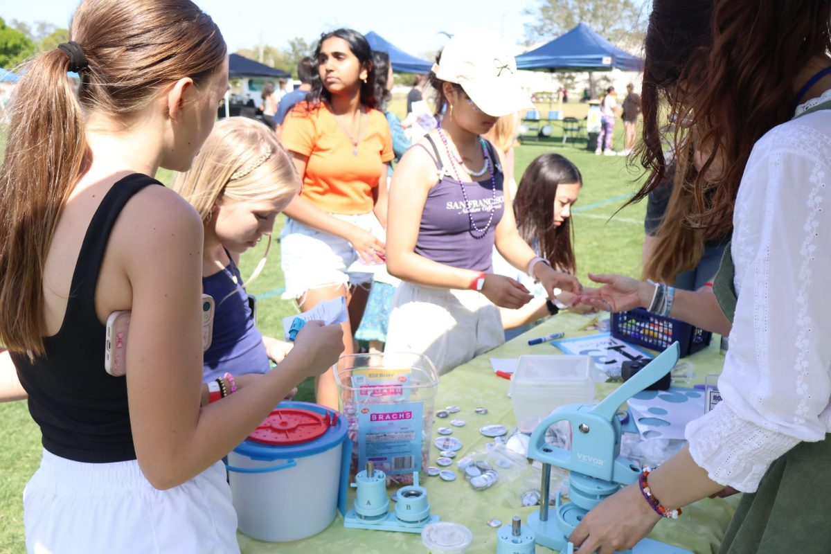 Students create customized pins at the 'Roar' newspaper table. Senior Cat Pelli (right) took photos on a camera, which were printed out and embedded onto blank pins.